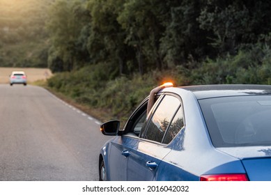 hand placing the new V16 emergency light, which replaces the emergency triangles, broken blue vehicle stopped on the road and with another car in the background - Shutterstock ID 2016042032