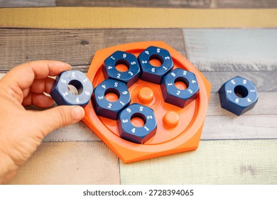 Hand placing numbered blue hexagonal puzzle pieces orange educational game board, developing logic and math skills, STEM toy, mental exercise, cognitive development, problem solving, matching numbers