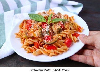 Hand Placing A Plate Of Delectable Fusilli Pasta In Marinara Sauce On Wooden Table