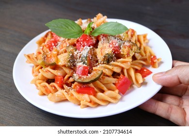 Hand Placing A Plate Of Mouthwatering Wholemeal Fusilli Pasta In Tomato Sauce On Wooden Table