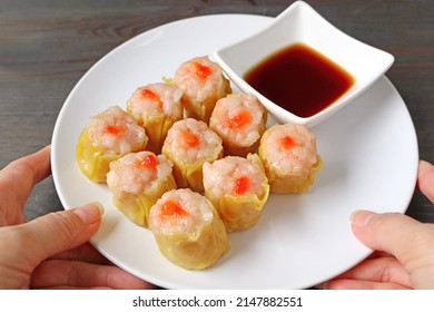 Hand Placing A Plate Of Shrimp And Pork Filled Chinese Steamed Dumplings Or Shumai On Wooden Table