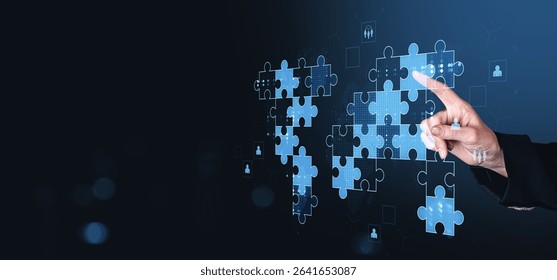 Hand placing puzzle pieces forming a glowing digital world map, modern futuristic style, on a dark blue background. Concept of global teamwork success