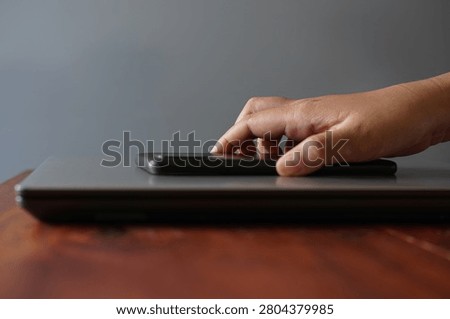 Hand placing a smartphone face down on a closed laptop. Minimalist workspace representing digital wellbeing, focus, work break, or productivity concept