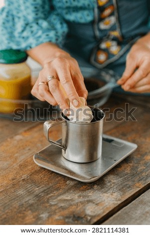 Hand placing solid ingredient into metal cup on digital scale during homemade preparation on rustic wooden table