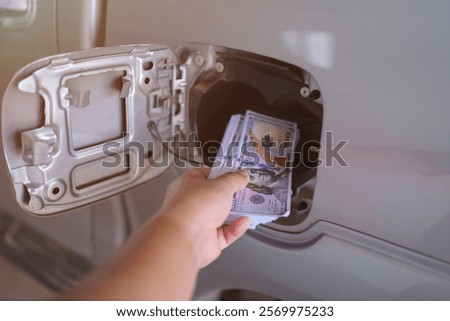 A hand placing a stack of fake dollar bills into a car's fuel compartment. Economy concept.