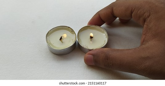 Hand Placing Two Wax Candles With Flame Lit On Occasion Of Deepavali Hindu Festival Of Light Isolated On White Table Background Arranged In Order With Selective Focus On Candle. Closeup Macro Top View