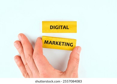 A hand is placing two yellow blocks next to each other. One block has the word 'Digital' and the other 'Marketing', highlighting the concept of online promotional strategies.