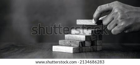 Hand is placing wood block tower stack in pyramid stair step with caution to prevent collapse or crash concepts of financial risk management and strategic planning and business challenge plan.
