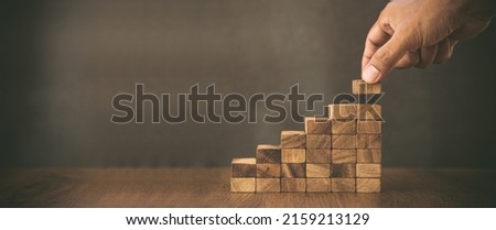Hand placing wood block tower stack in pyramid stair step with caution to prevent collapse or crash concepts of financial risk management and strategic planning and business challenge plan.