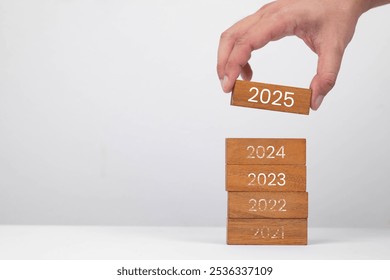 A hand placing a wooden block labeled '2025' on top of stacked blocks representing previous years. Symbolizes progress and planning. - Powered by Shutterstock