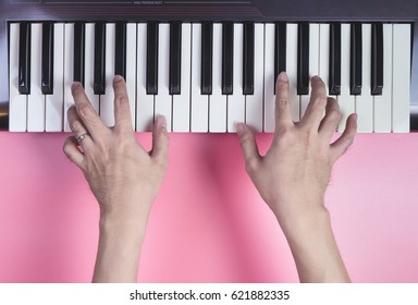 Hand playing Music keyboard on pink background, above view.