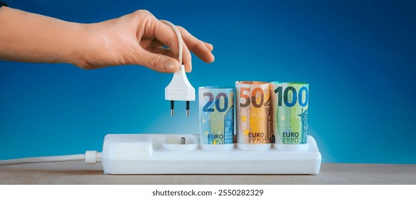 hand plugging an electric cable into a power . Euro money paper banknotes plugged into a white power strip Increasing cost of electricity for business users and residential customers. Rise in electric