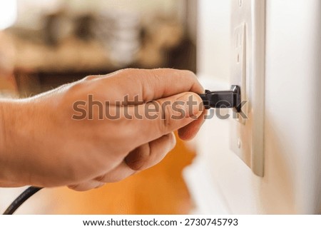 Hand plugging power cable into American wall outlet on interior wall with soft natural light and shallow depth of field. High quality photo