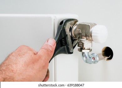 Hand of plumber using a wrench on a radiator valve