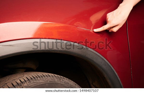 Hand pointing\
at dent on red car close up\
view