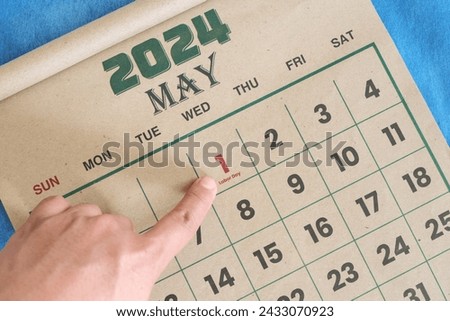 Hand pointing on May 1 2024 date on calendar flat lay in blue background. Labor day or International workers day celebration reminder.