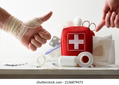 Hand pointing at travel portable first aid bag full of medical objects and tools with bandaged hand with ok sign. Front view. Horizontal composition