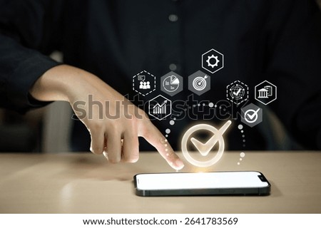 A hand points to a glowing checkmark icon on a smartphone screen, with various business-related icons floating around.