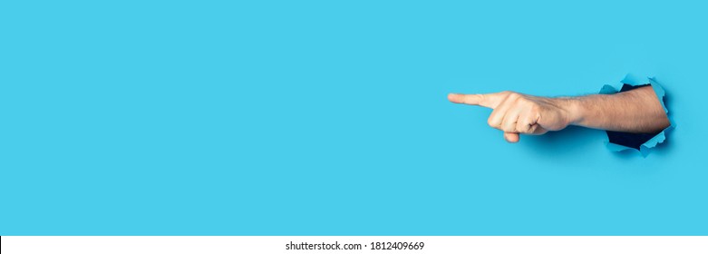 Hand points to something on a blue background. Gesture look at this, pay attention