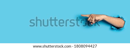 Hand points to something on a blue background. Gesture look at this, pay attention