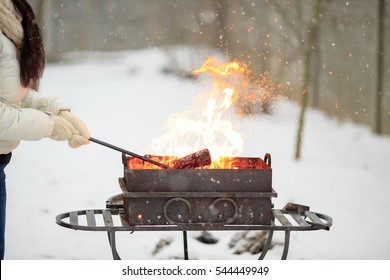 Hand with poker adjusts the coals in the brazier. Lighting the barbecue in the backyard in the winter.