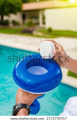 Hand of a pool disinfection worker holding a dispenser with a chlorine tablet. Hands holding a dispenser with pool chlorine tablet, pool float and chlorine tablets for pool maintenance. 