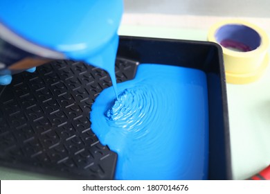 Hand Pour Blue Paint From Can Into Black Plastic Tray. In Background There Are Two Masking Tape Of Different Width.