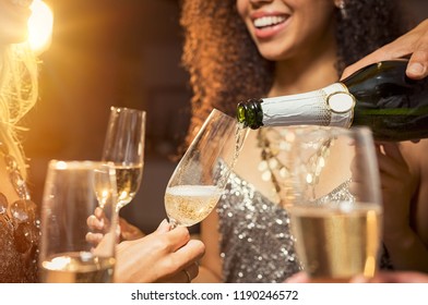 Hand pouring champagne from bottle into glasses with friends around him. Closeup of hand pouring white wine in flutes during party. Detail shot of new year’s eve celebration.