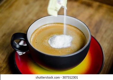 Hand Pouring Creamer In To A Cup Of Coffee On Wooden Background.