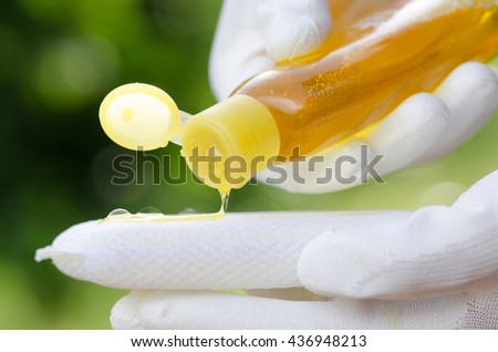 Hand pouring dish washing liquid on sponge over nature green background