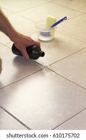 Hand Pouring Hydrogen Peroxide On Bathroom Floor Tile Grout. Putting Hydrogen Peroxide On Floor Grout With Baking Soda, Scrub Brush And Scrub Sponge In Back.