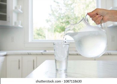 A Woman'??s Hand Pouring Ice Water From A Pitcher Into A Glass.