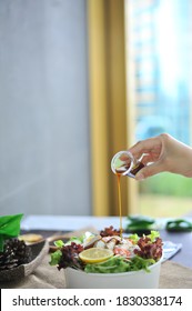 A Hand Pouring Salad Dressing Into A Garden Salad Bowl