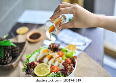 A Hand Pouring Salad Dressing Into Garden Salad