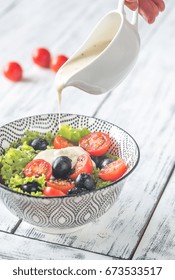 A Hand Pouring Salad Dressing Onto Caesar Salad