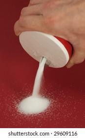 A Hand Pouring Salt On A Red Background