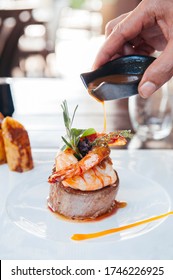 Hand Pouring Sauce Onto Beef Fillet Mignon Steak And Grill Shrimp On White Plate