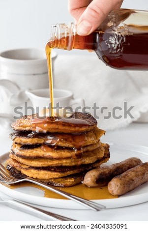 A hand pouring syrup onto a freshly made stack of sweet potato pancakes.