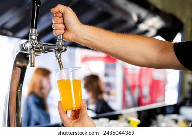 A hand pours beer from a tap into a clear plastic cup at a bar or public event. - Powered by Shutterstock