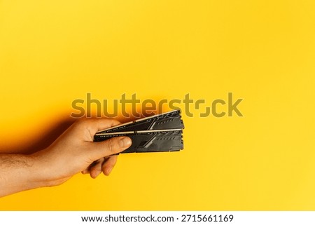 Hand presenting stack of desktop RAM modules on yellow background