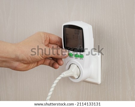 Hand presses button in wattmeter on wall, for measuring electricity costs in device, close-up