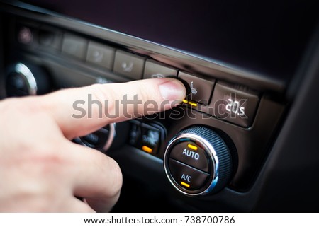 Hand pressing the button for heated seats in the car