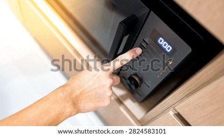 Hand pressing button setting mode and timer on modern black microwave oven in wooden cabinet. Using home appliance in the kitchen