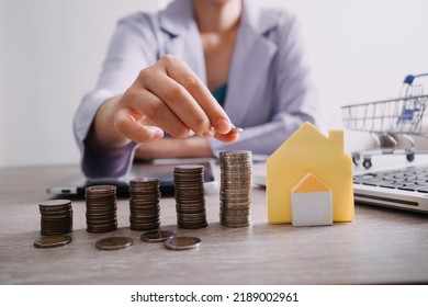 The Hand Is Pressing Calculators, Piggy Bank With Wooden House. Buy Or Rent Question On Note With Calculators On Desk. Save Money And Buy House Concept.