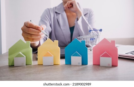 The Hand Is Pressing Calculators, Piggy Bank With Wooden House. Buy Or Rent Question On Note With Calculators On Desk. Save Money And Buy House Concept.