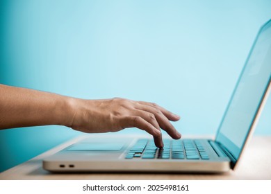 Hand Pressing Computer Keyboard. Side View. Closeup shot and Selective Focus on Finger. Person using Laptop for Working on Desk against the Blue Wall. Clean and Minimal photo - Powered by Shutterstock