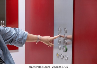 Hand is pressing an elevator button in a stylish building with vibrant red walls, highlighting modern architecture and user engagement in urban space