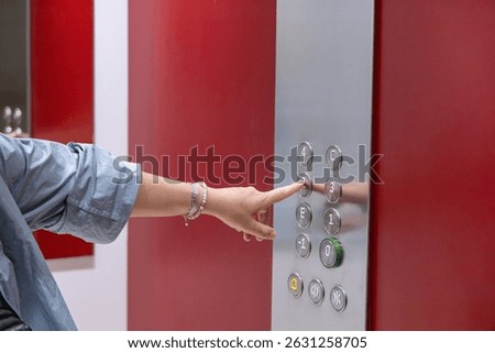 Hand is pressing an elevator button in a stylish building with vibrant red walls, highlighting modern architecture and user engagement in urban space