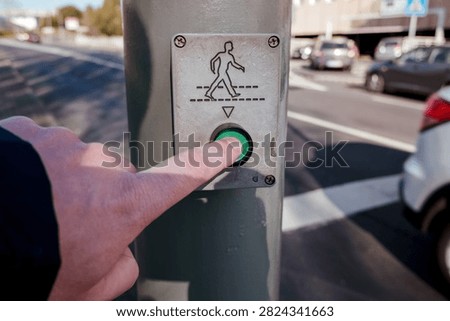 Hand pressing green button on a pedestrian crossing signal for urban road safety