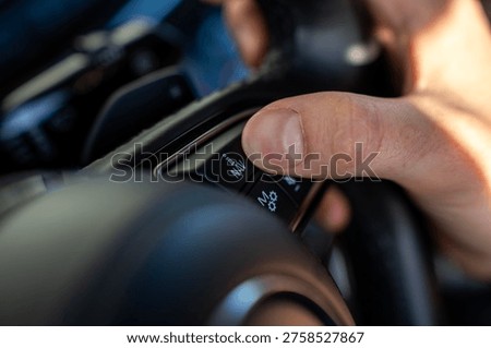 Hand pressing navigation button on car steering wheel, close up of control panel with NAV icon, automotive interior detail.